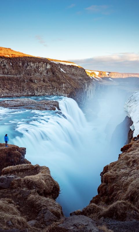 person standing on cliff near large waterfalls und... wallpaper