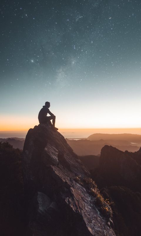 silhouette of person sitting on rock formation dur... wallpaper