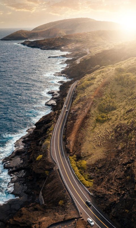 vehicles passing on road beside body of water duri... wallpaper
