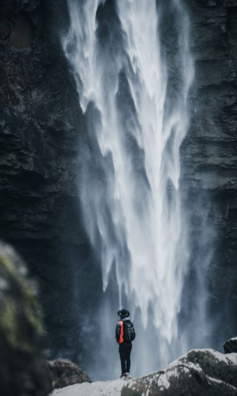 man standing near waterfalls wallpaper