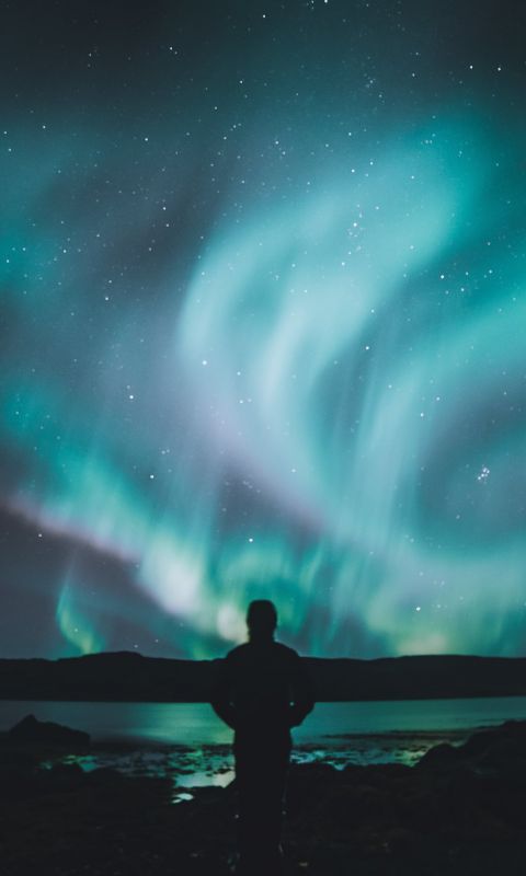 person standing on ground under sky lights wallpaper